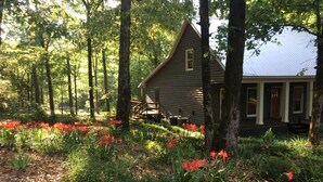 A cabin surrounded by a forest with a wooden deck and a covered porch. - Natchez Trace Cabin Retreat on 5 acres (Canton)