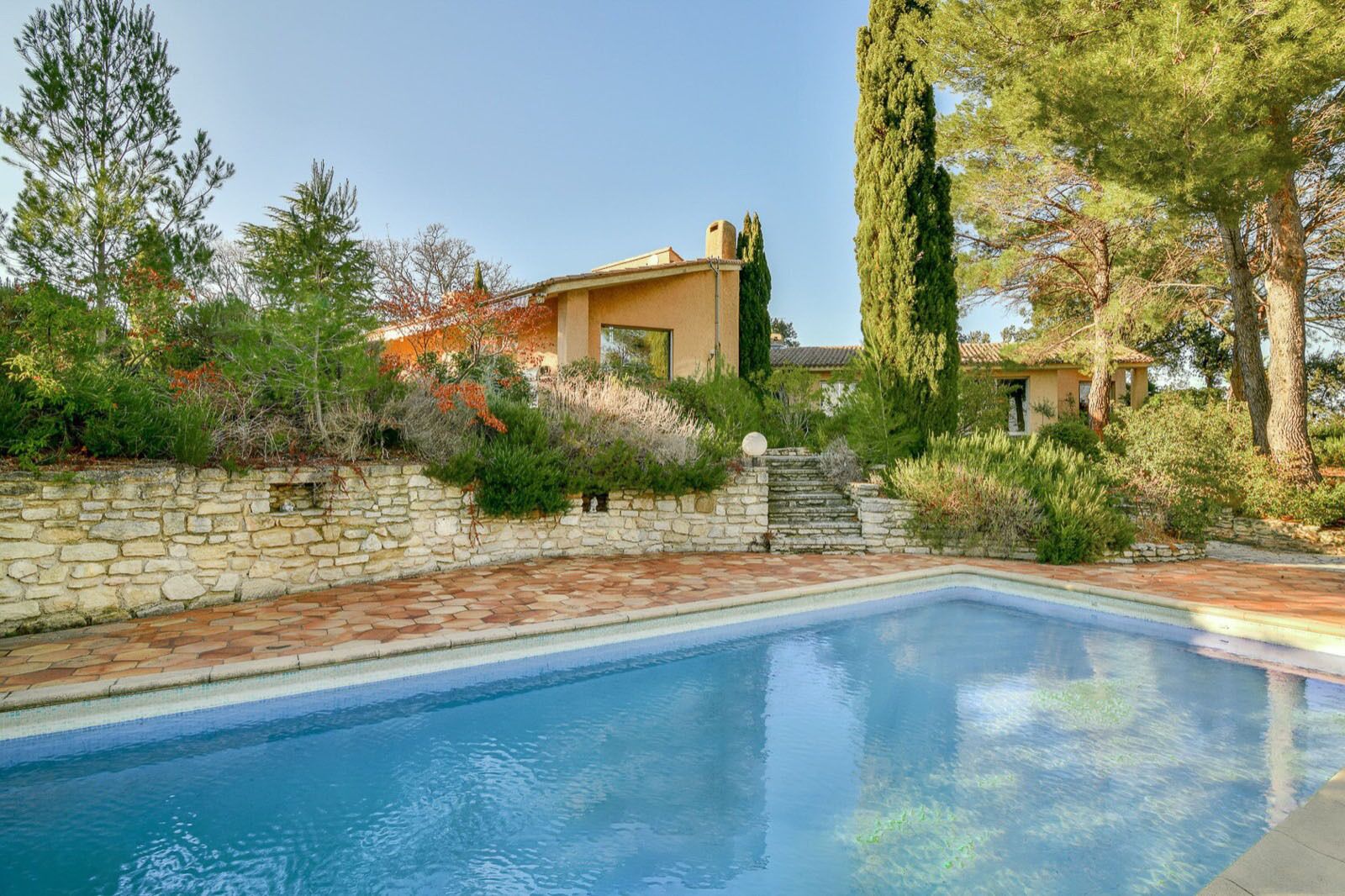 Une piscine avec un mur en pierre et des marches menant à une maison.