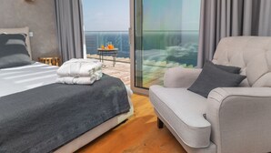 Een moderne hotelkamer met een bed, een bank, een klein tafeltje met drankjes en een balkon met uitzicht.