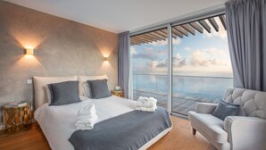 Een moderne hotelkamer met een groot bed, een zithoek en een balkon met uitzicht op zee.