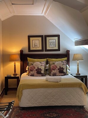 Una cama bien hecha con almohadillas florales, un edredón acolchado y un cabecero de madera. Encima de la cama hay dos cuadros enmarcados en la pared.