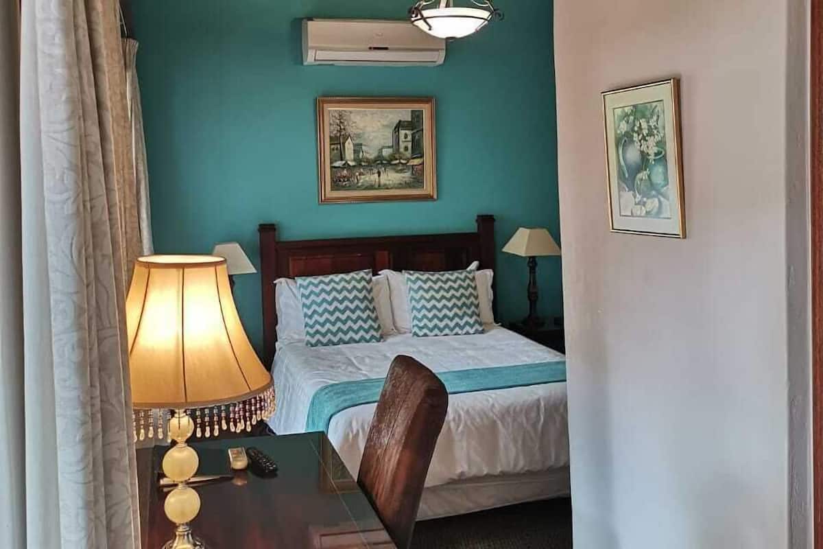 Ein Zimmer mit Holzboden, einem Bett mit Holzgestell, einem Schreibtisch mit Lampe und zwei gerahmten Bildern an der Wand.