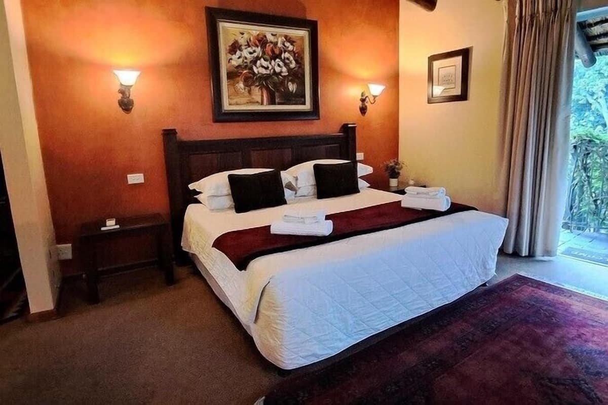 Ein Hotelzimmer mit einem großen Bett, zwei Nachttischen, einem Wandbild und Blick auf Grünfläche draußen.