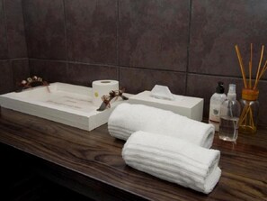 Una encimera de baño con una toalla blanca, una botella de jabón para manos, un dispensador de gel antibacterial y un difusor de cañas.