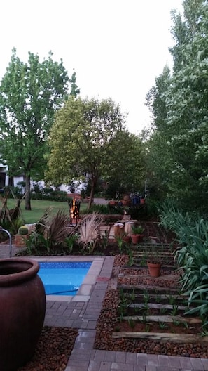 Un jardín ajardinado con piscina, plantas en macetas y un pozo de fuego.