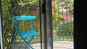 Zona de porxo coberta amb taula i caires blaus plegables, barana metàl·lica i vista d'un jardí amb arbres i flors roses.