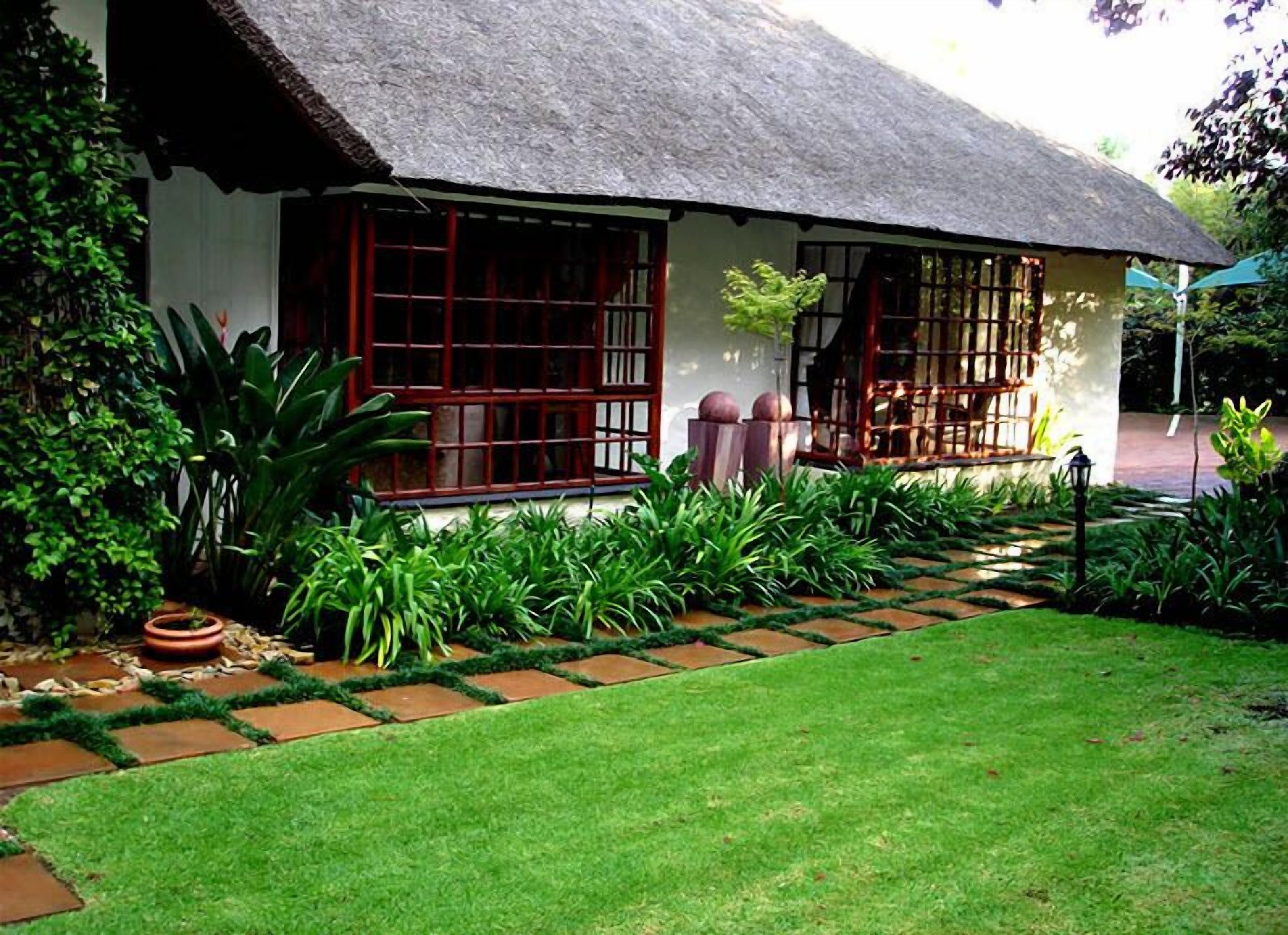 A traditional house with a thatched roof, large windows, and a well-maintained garden with a stone pathway.