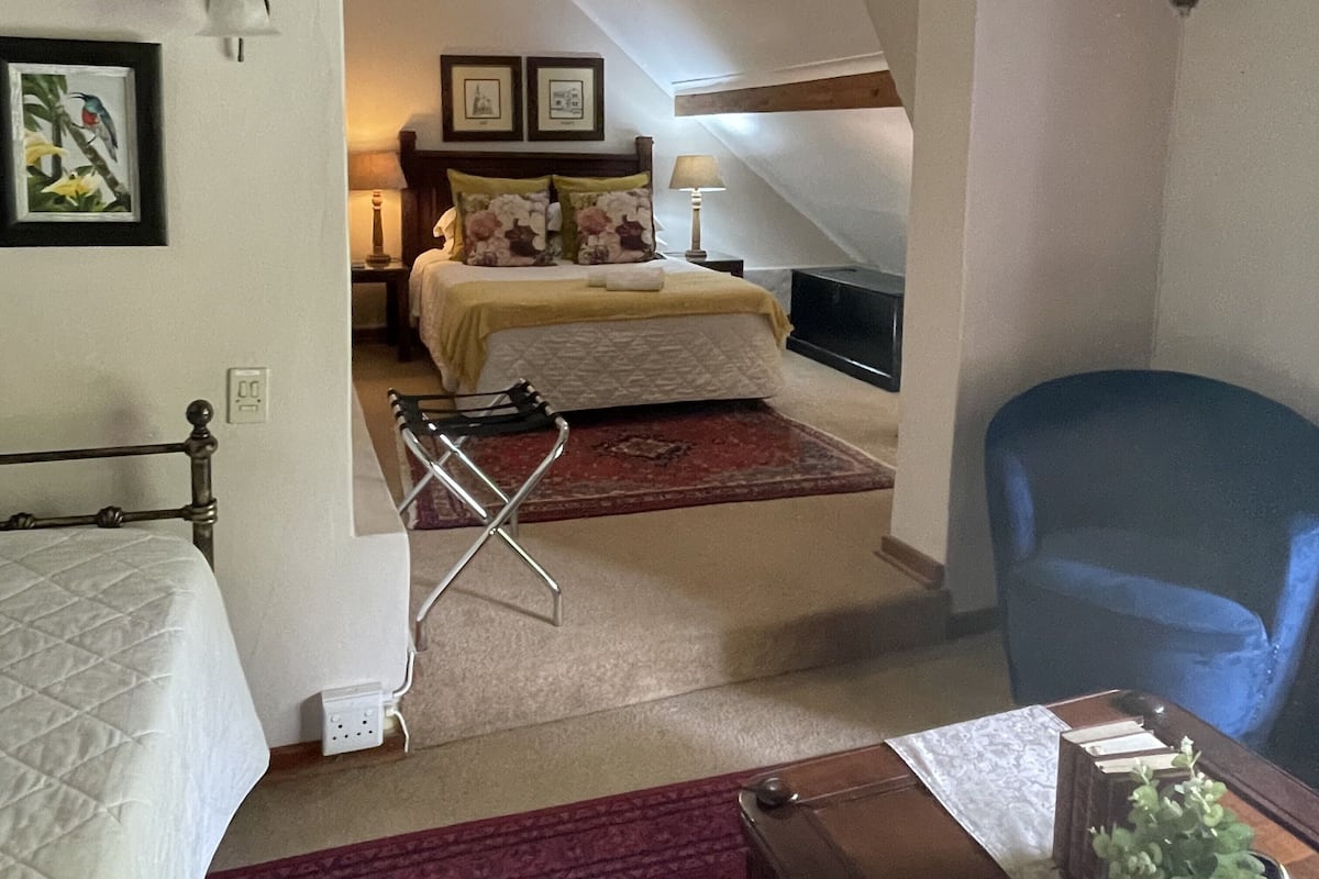 Ein Schlafzimmer mit einem Bett, einem Sessel, einem Schreibtisch und einem kleinen Tisch mit Büchern und einer Pflanze.