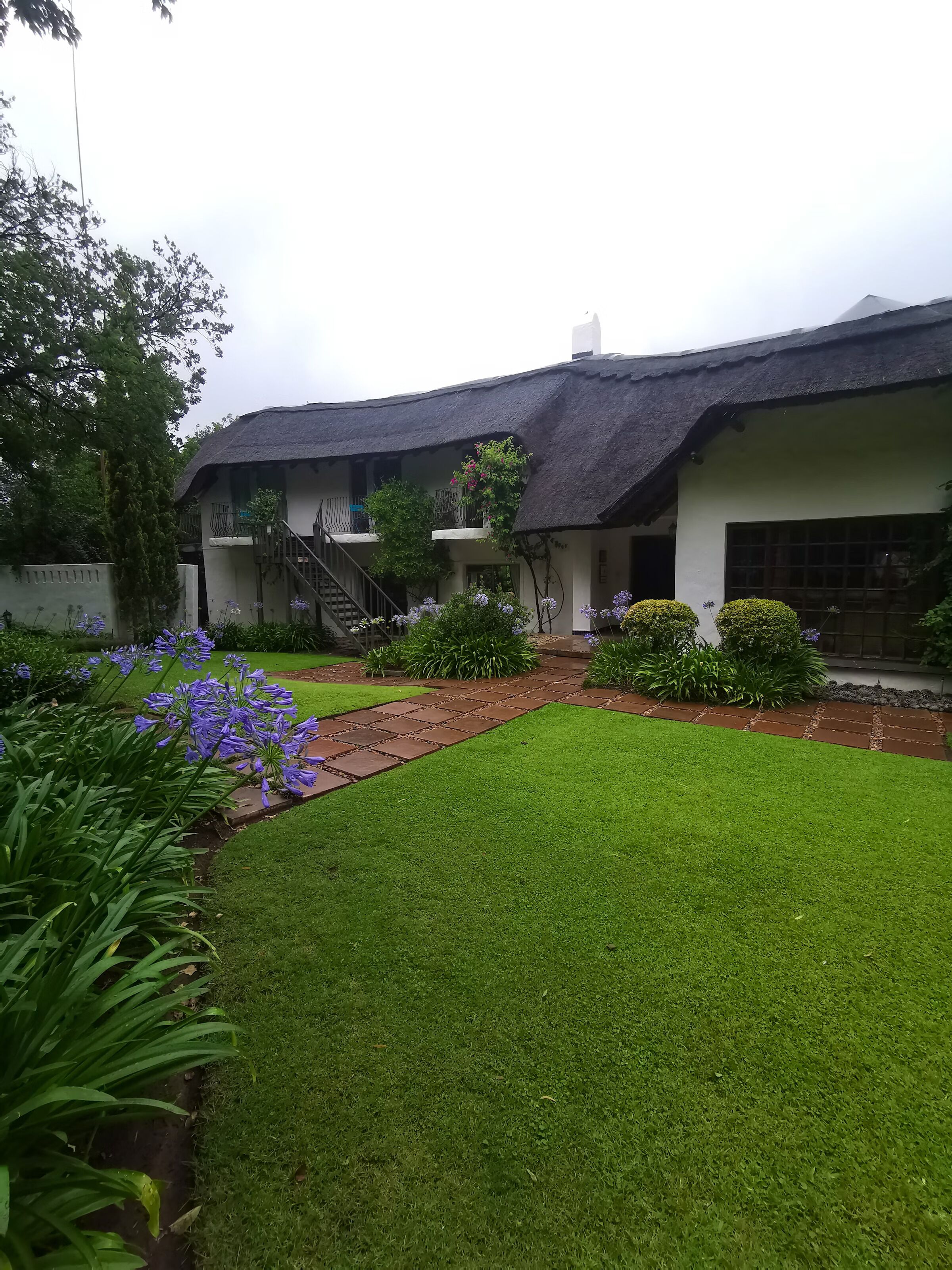 A traditional building with a thatched roof, a well-maintained lawn, and a variety of flowering plants.