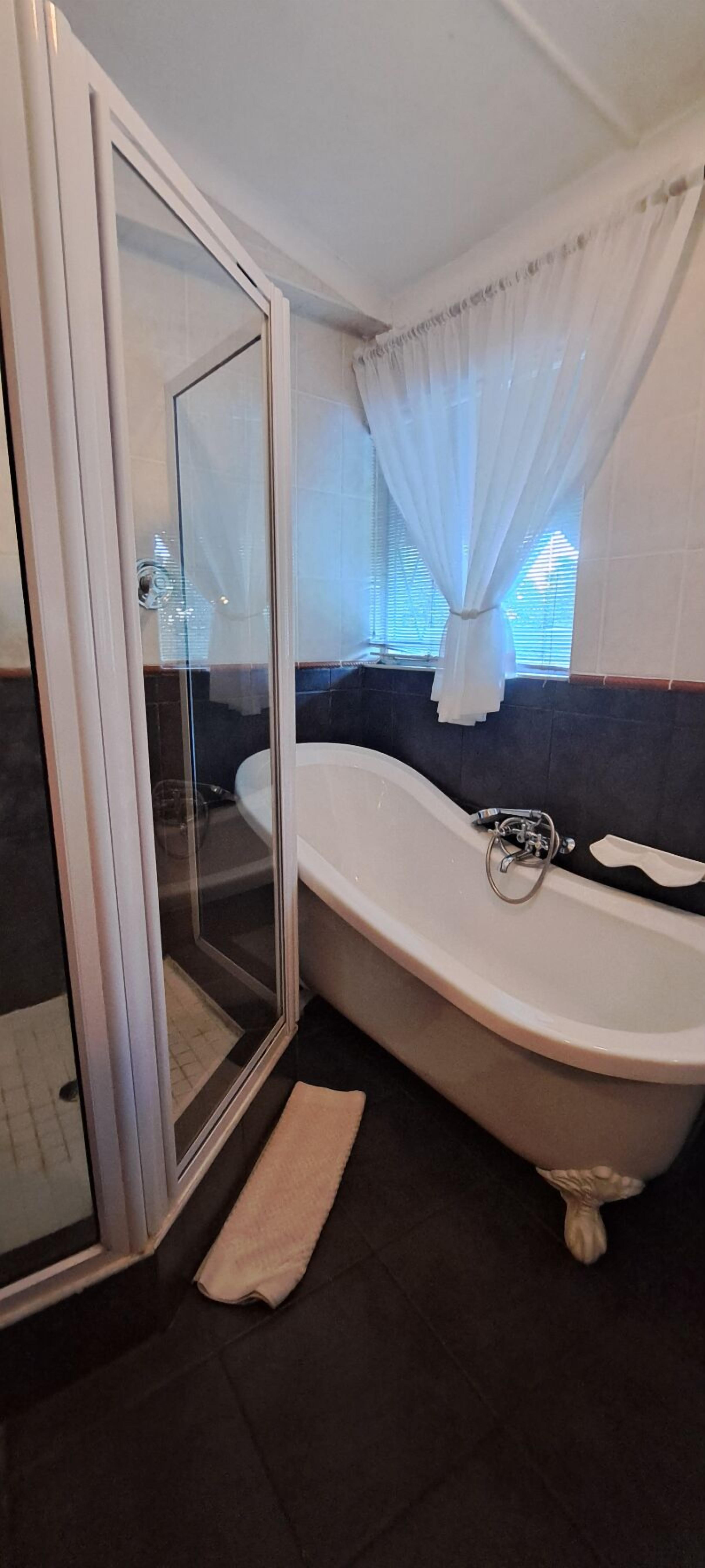 Ein Badezimmer mit einer Duschkabine, einer freistehenden Badewanne und einem Fenster mit weißen Vorhängen.