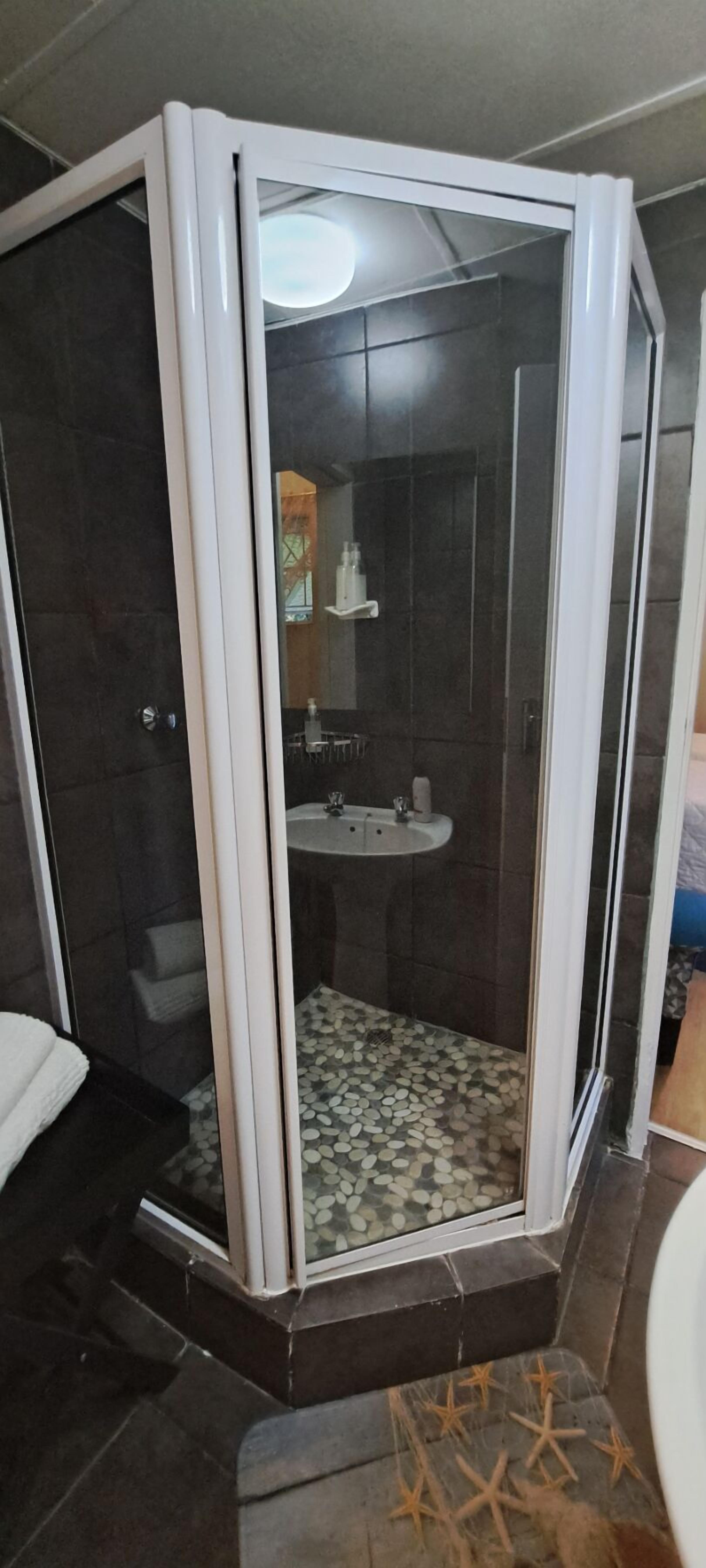 A corner shower enclosure with a glass door, a sink, and a tiled floor.