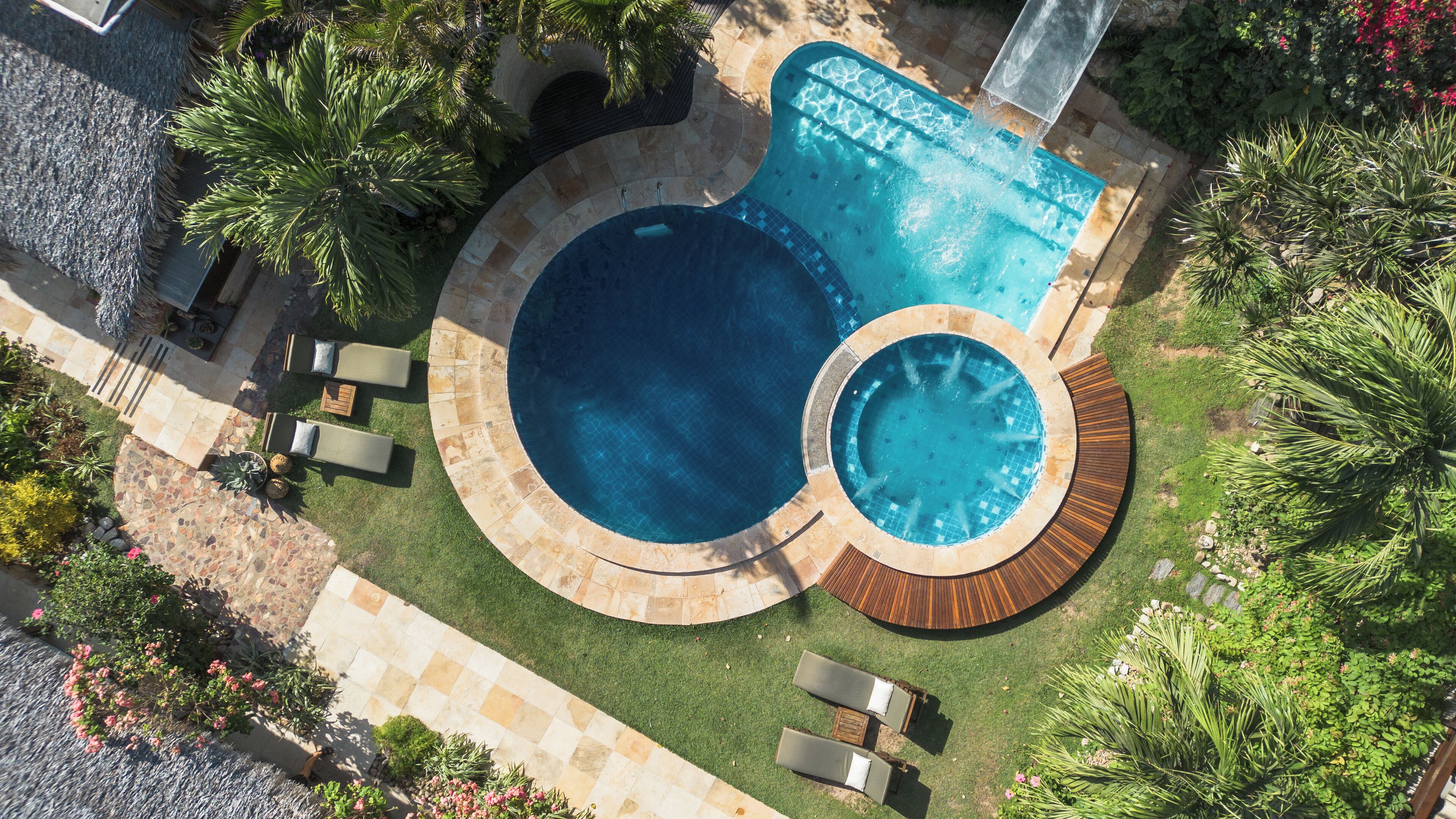 A circular pool with a hot tub, surrounded by lounge chairs and palm trees.