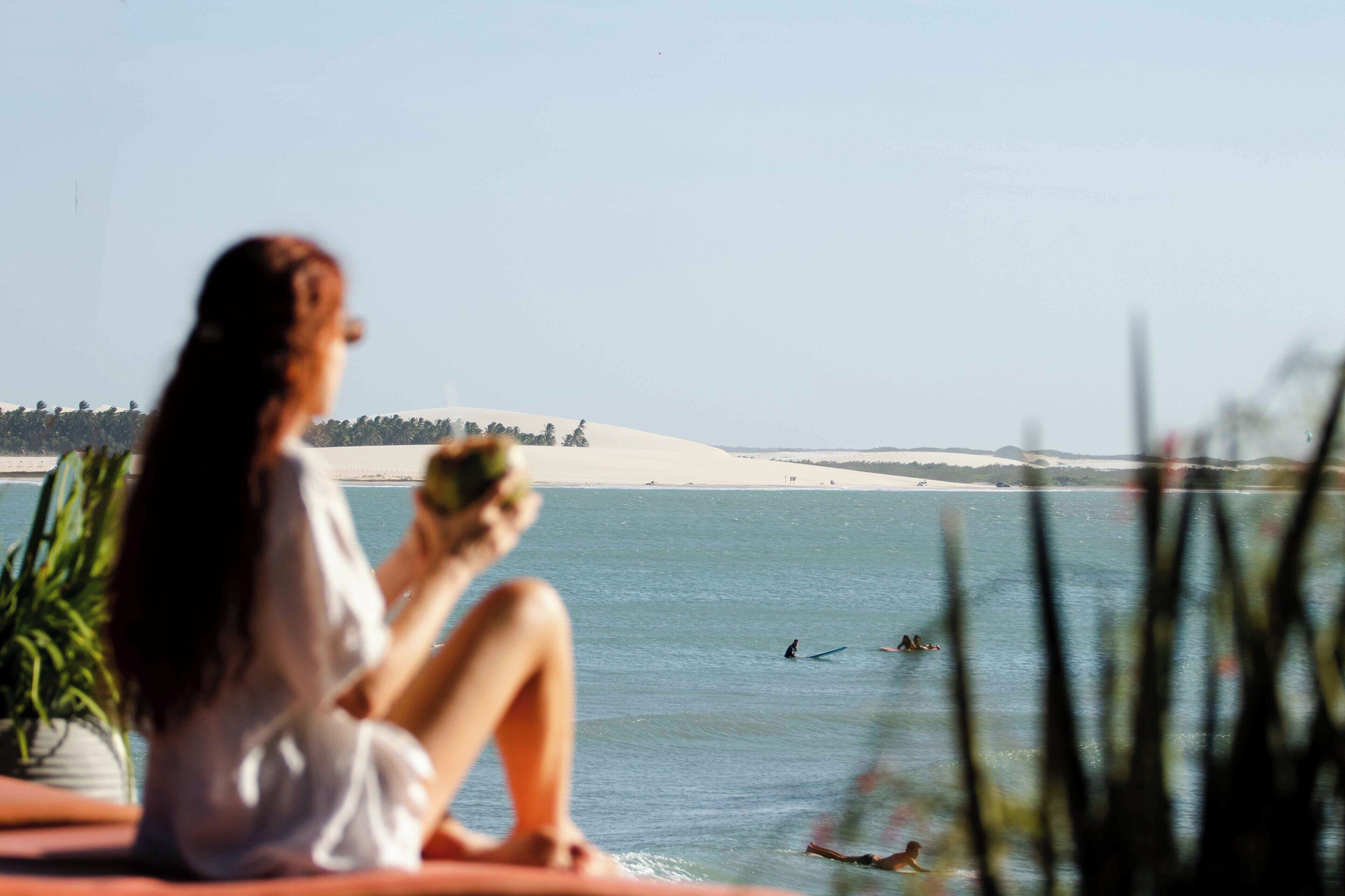 A person sitting by a body of water with a view of a beach and dunes in the distance.