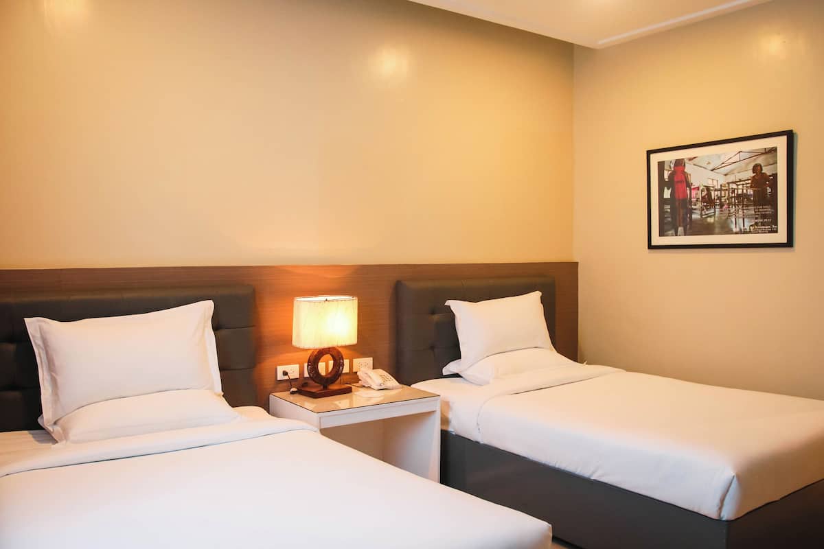 A hotel room with two single beds, a nightstand with a lamp, a phone, and a framed picture on the wall.