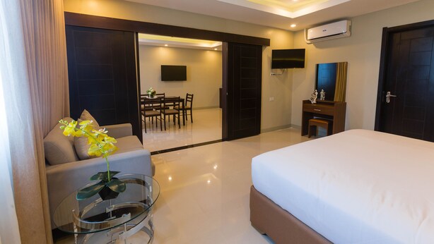 A modern hotel room with a bed, a sofa, a dining table, and a TV.