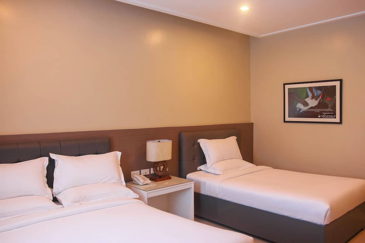 A hotel room with two single beds, a nightstand with a lamp, and a framed picture on the wall.