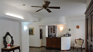 A spacious lobby with a reception desk, a wooden chair, a ceiling fan, and a stone-tiled floor. - Hotel Capri (Lesa)
