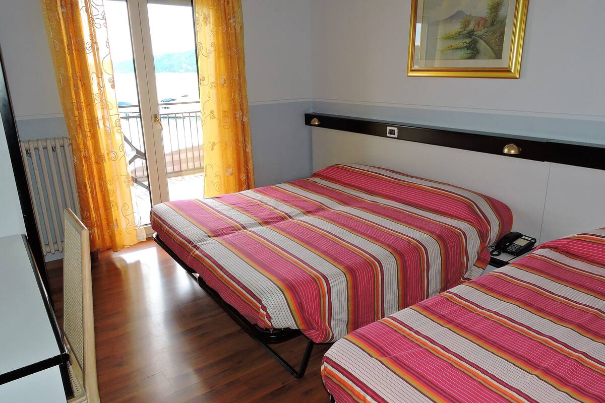 Quarto de hotel com duas camas, um radiador, uma janela com cortinas, um quadro na parede e um telefone na mesa de cabeceira.