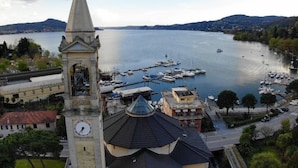 A church with a clock tower overlooking a marina with boats. - Hotel Capri (Lesa)