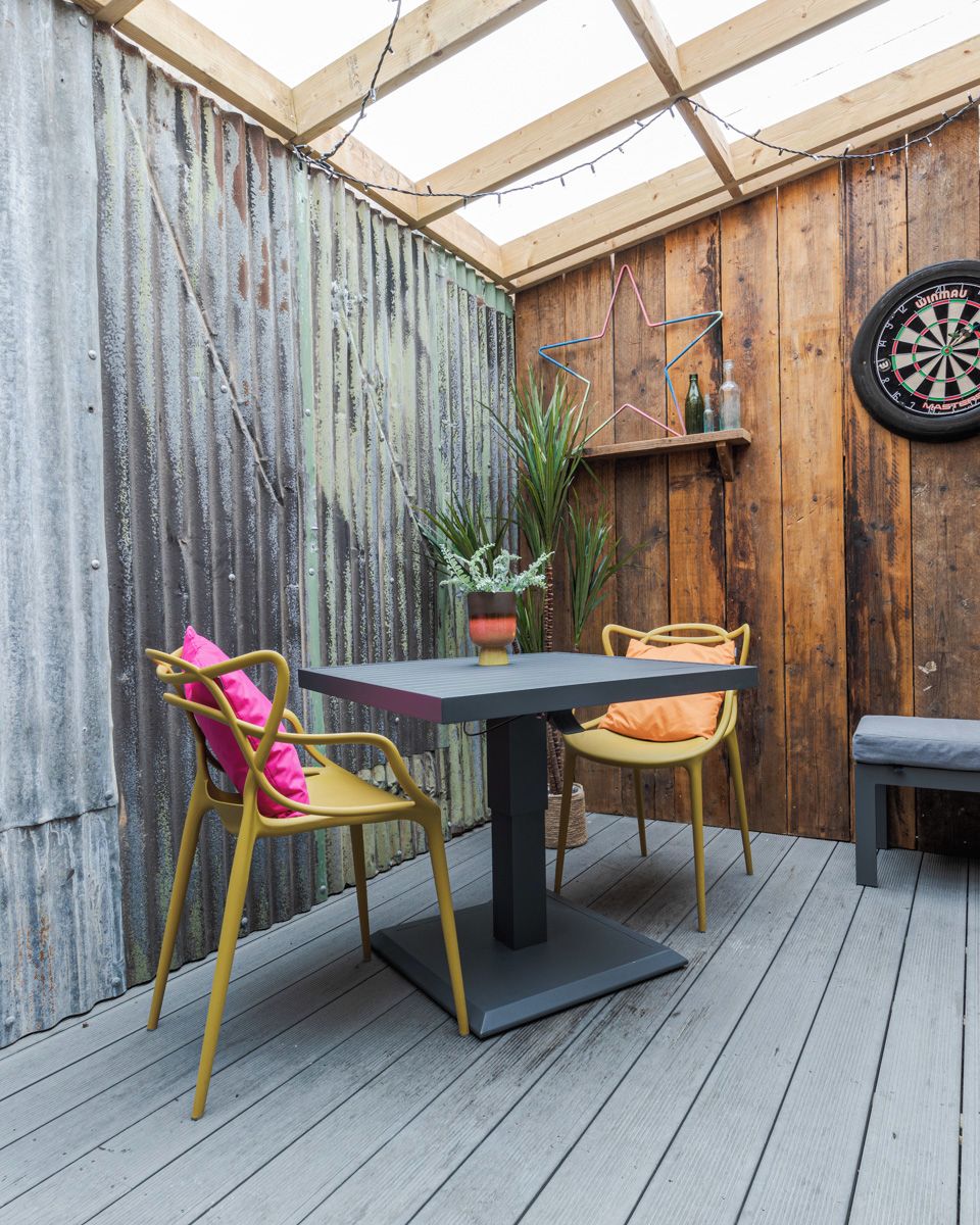 A wooden deck with a table and chairs, a dartboard, and a potted plant.