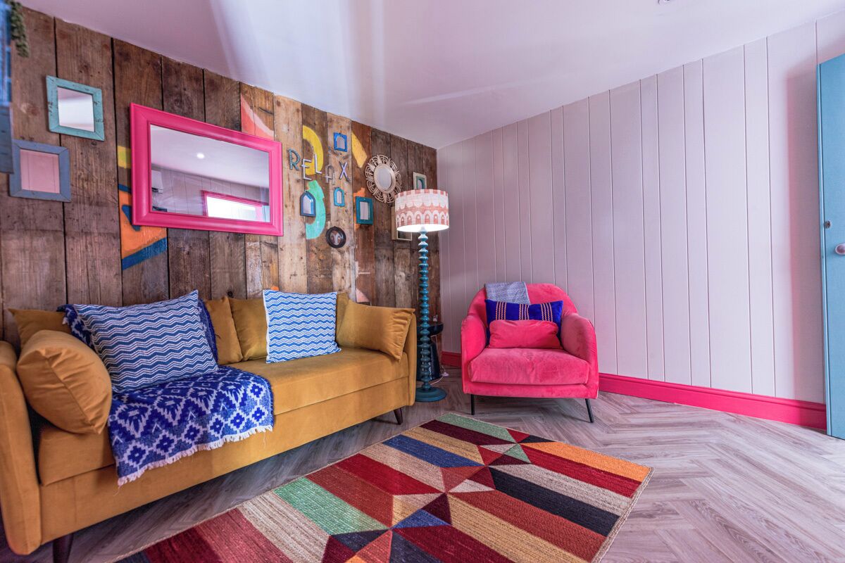 A room with a wooden wall, a sofa, a chair, and a patterned rug.