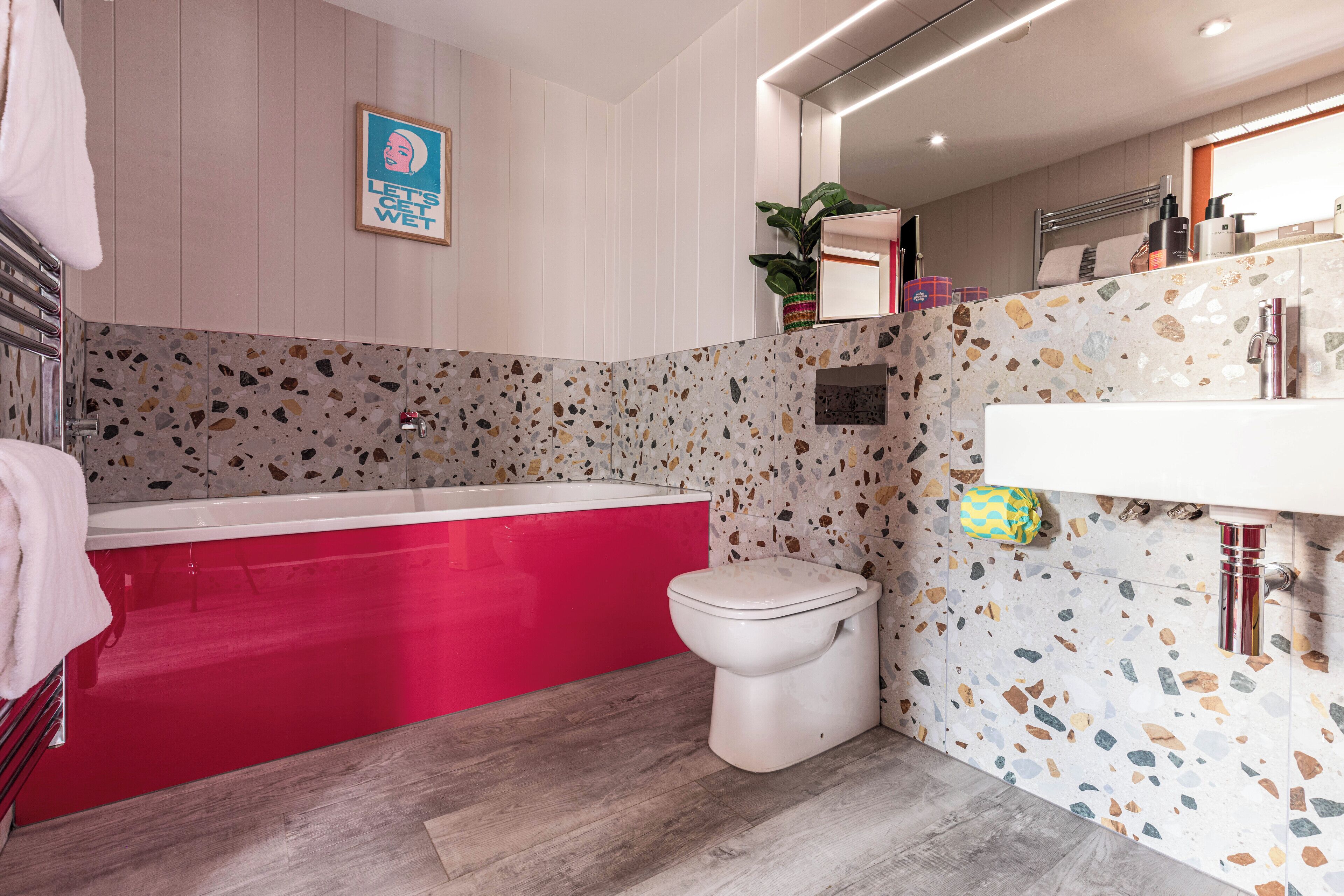 Un baño moderno con una bañera roja, inodoro blanco y paredes de terrazo.