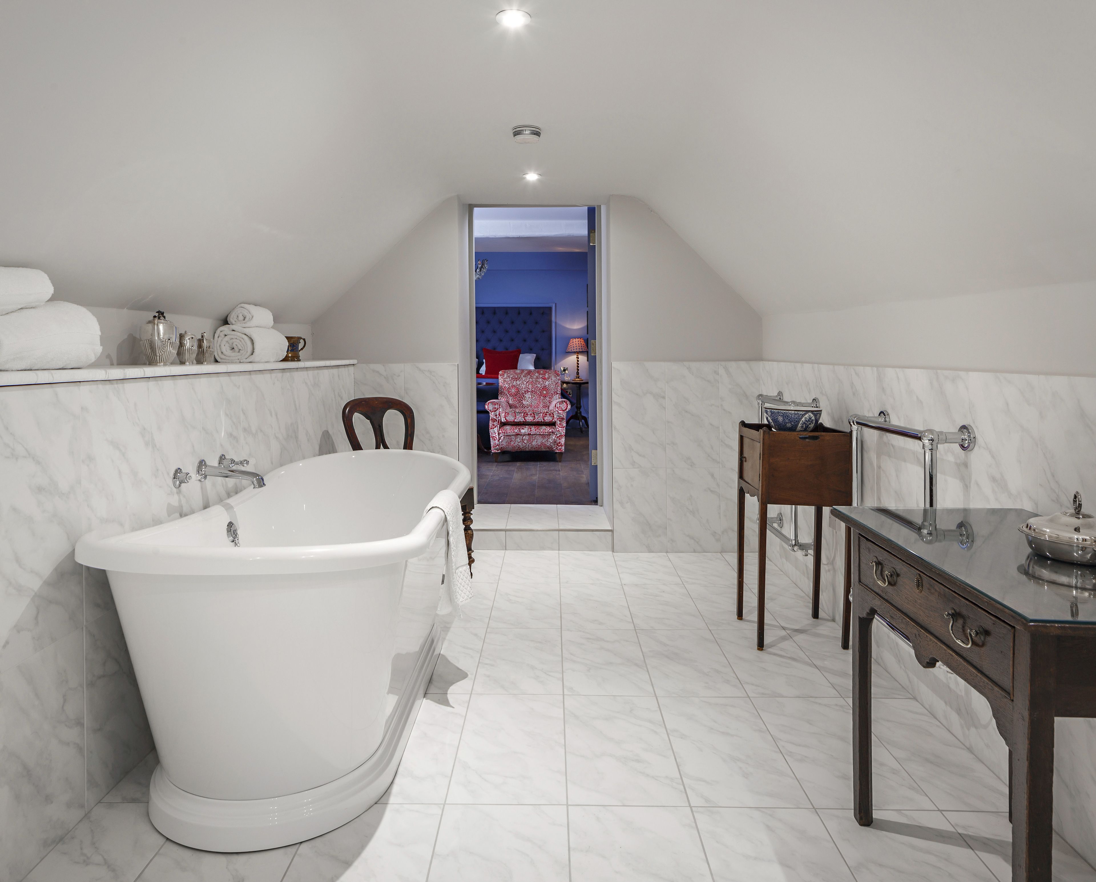 A modern bathroom with a freestanding bathtub, a vanity with a mirror, and a chair in the background.
