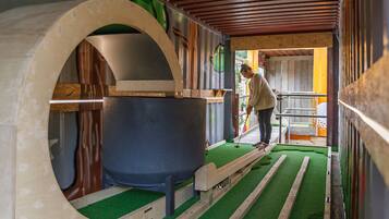 A room with a large circular structure, a wooden bench, and a green artificial turf floor.