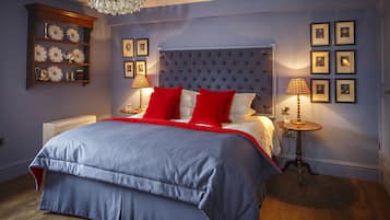 A bedroom with a large bed, a wooden dresser, a chandelier, and framed pictures on the wall.