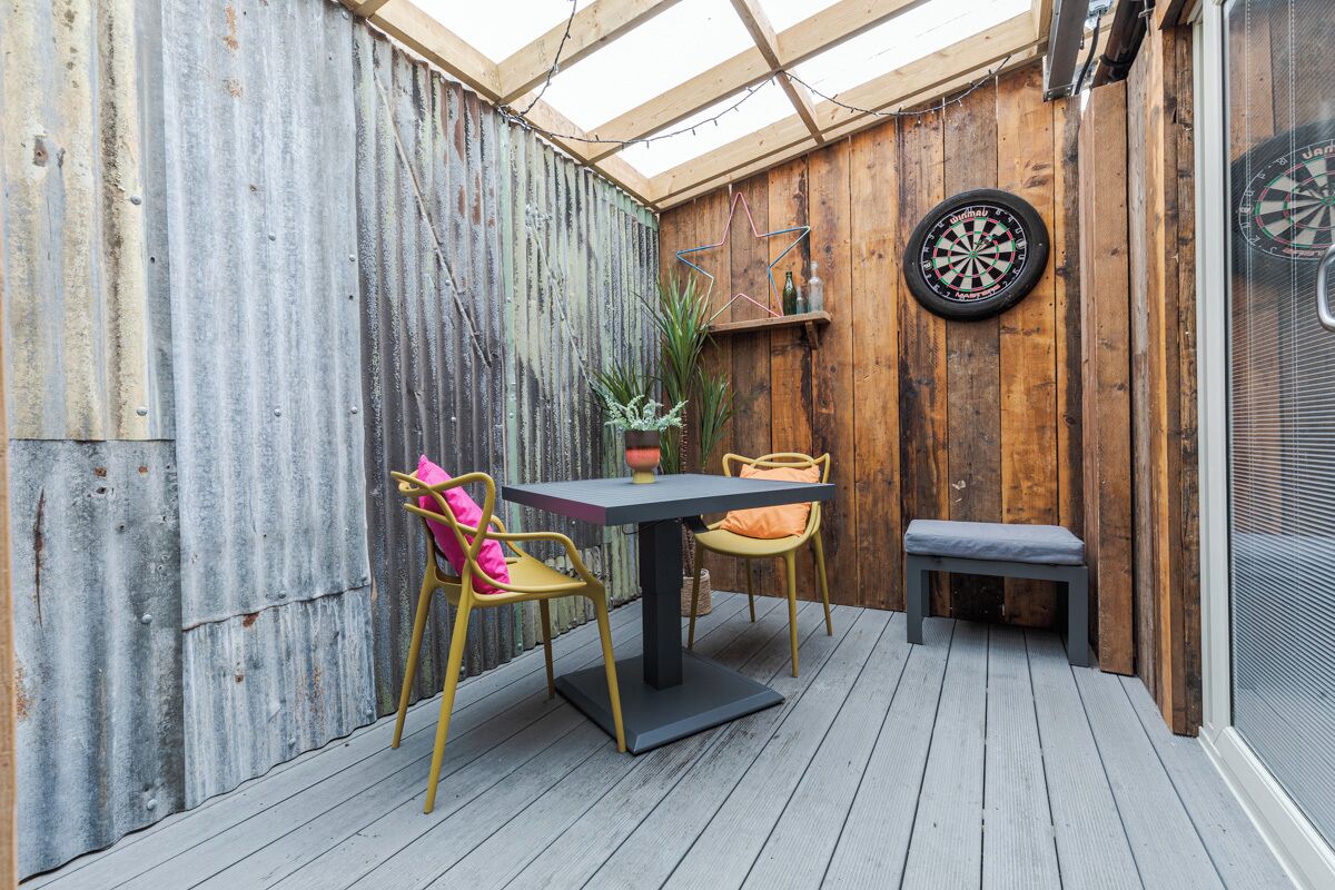 Een houten terras met een tafel, stoelen, een dartbord en een bloempot.