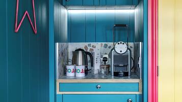 A kitchenette with a coffee machine, two mugs, a kettle, and a small cabinet.