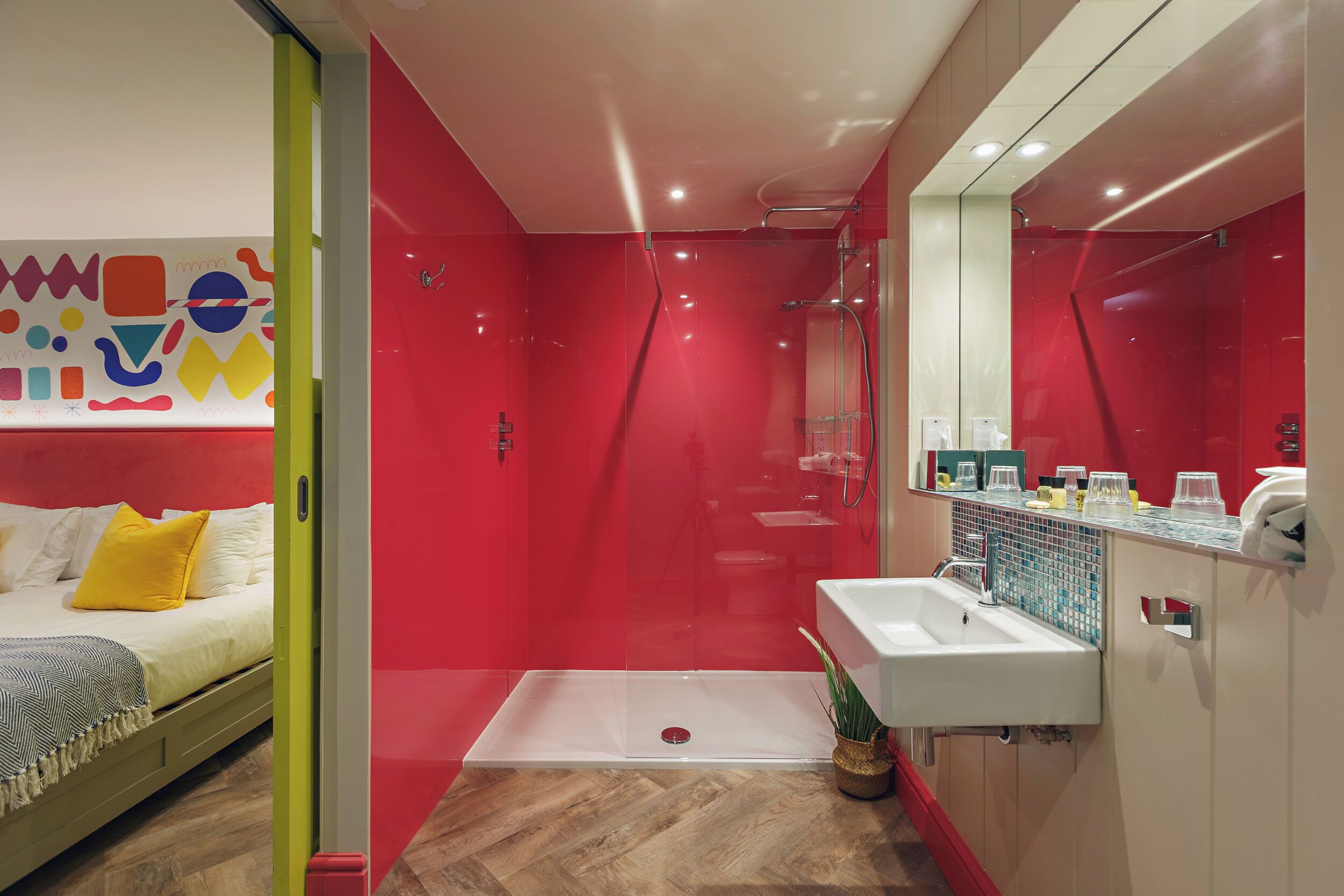 Een moderne badkamer met een douchecabine van glas, een witte wastafel en een bed met een geel kussen.