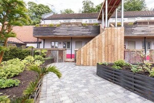 Un edificio residencial moderno con una terraza de madera y un sendero pavimentado.