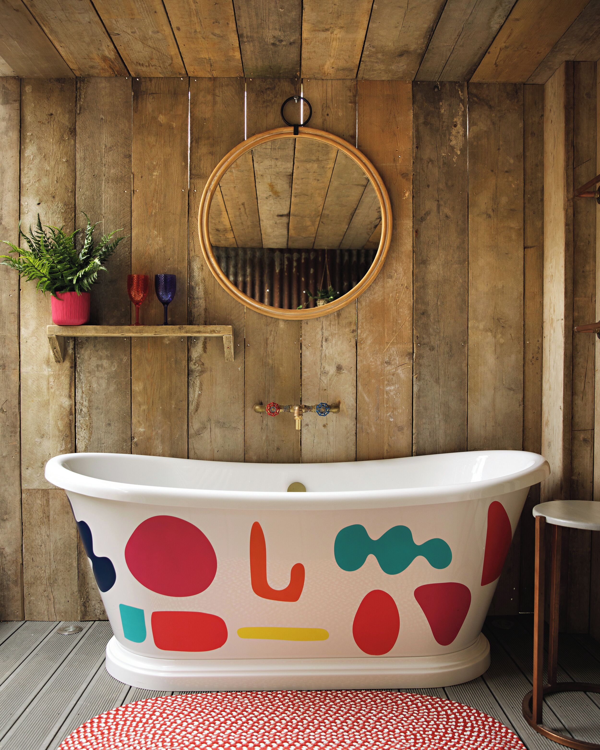 A bathroom with a freestanding bathtub, wooden walls, a mirror, and a small shelf with decorative items.