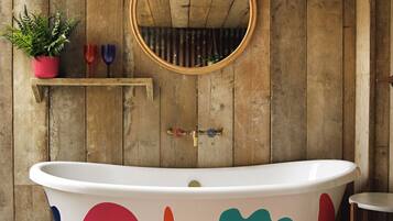 A bathroom with a freestanding bathtub, wooden walls, a mirror, and a small shelf with decorative items.
