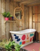 Un baño con una bañera independiente, paredes de madera, un espejo y una repisa con plantas.