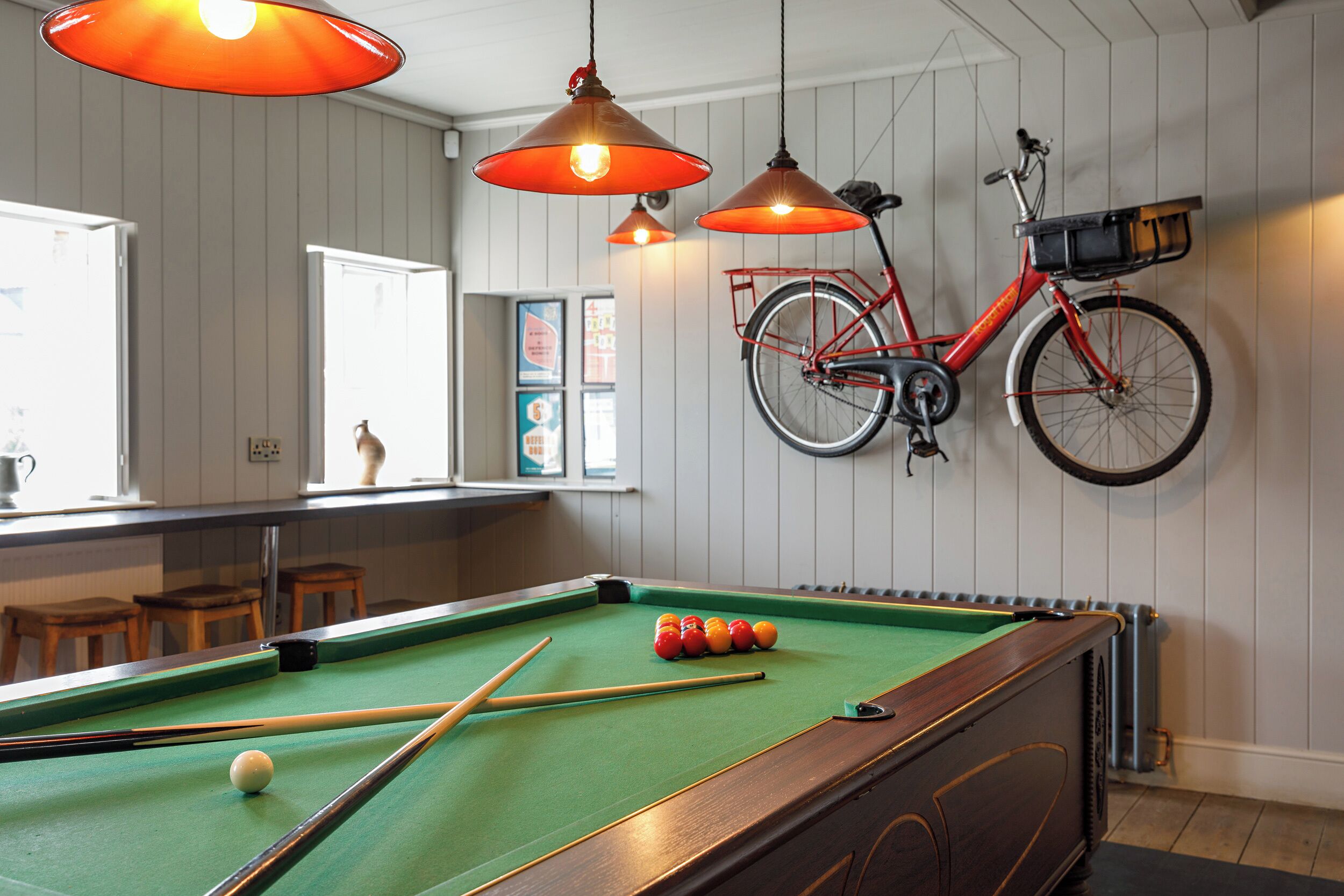 Ein Billardtisch mit Billardkugeln, ein an der Wand befestigtes Fahrrad und Holzschemeln.