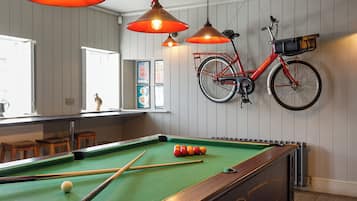 Ein Billardtisch mit Billardkugeln, ein an der Wand befestigtes Fahrrad und Holzschemeln.