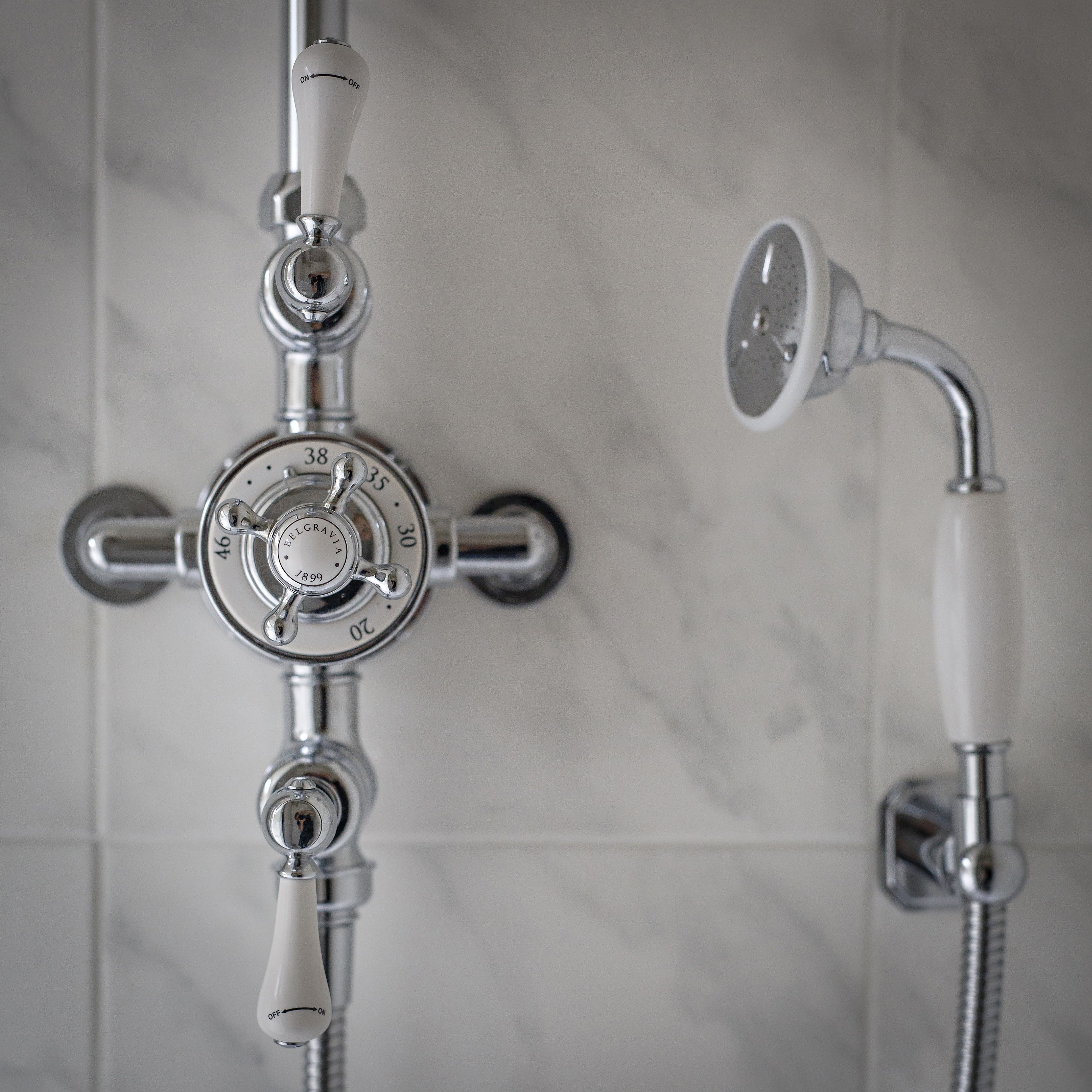 A bathroom with a modern shower system, including a control knob and a handheld showerhead.
