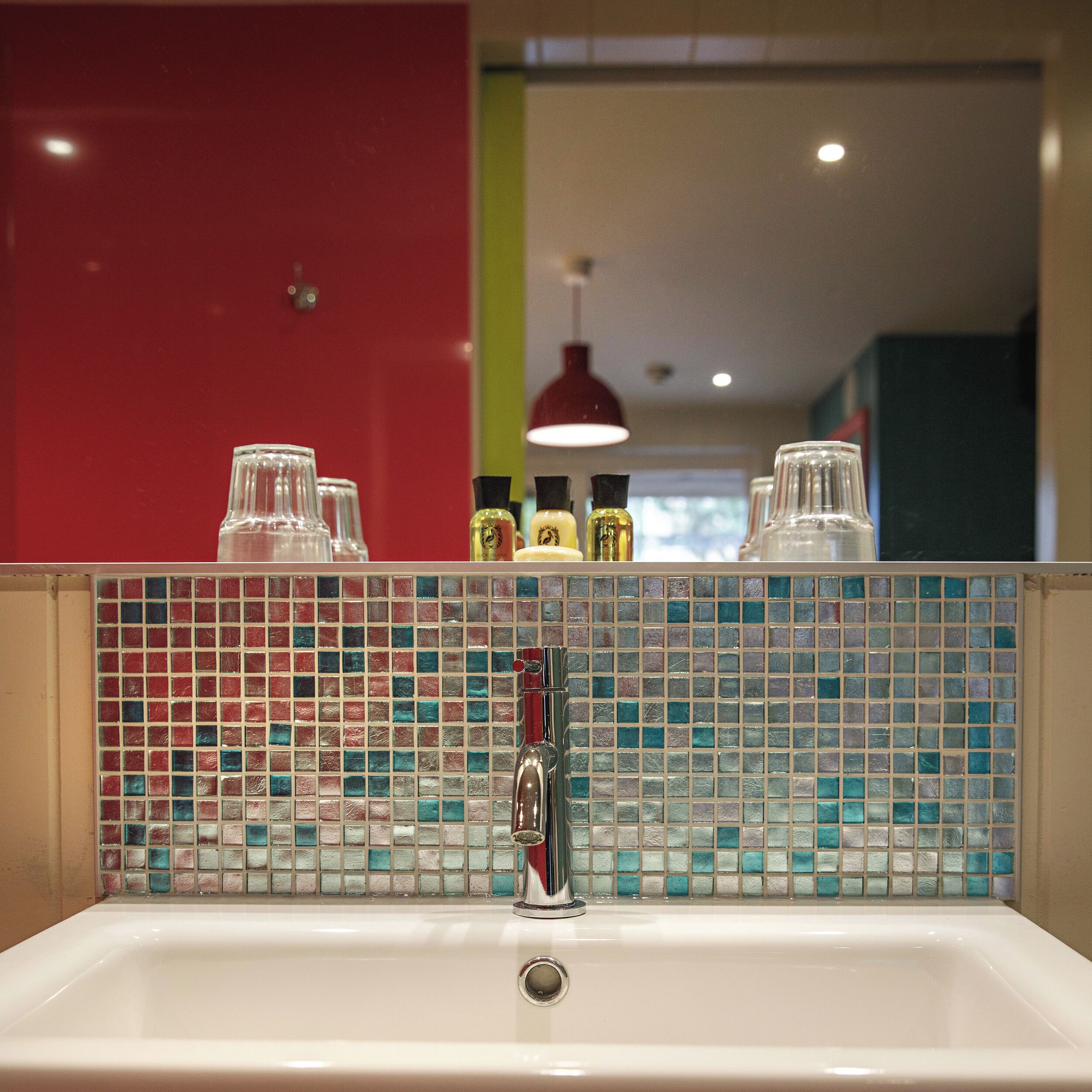 Une salle de bain avec un lavabo blanc, un miroir et un mur rouge.