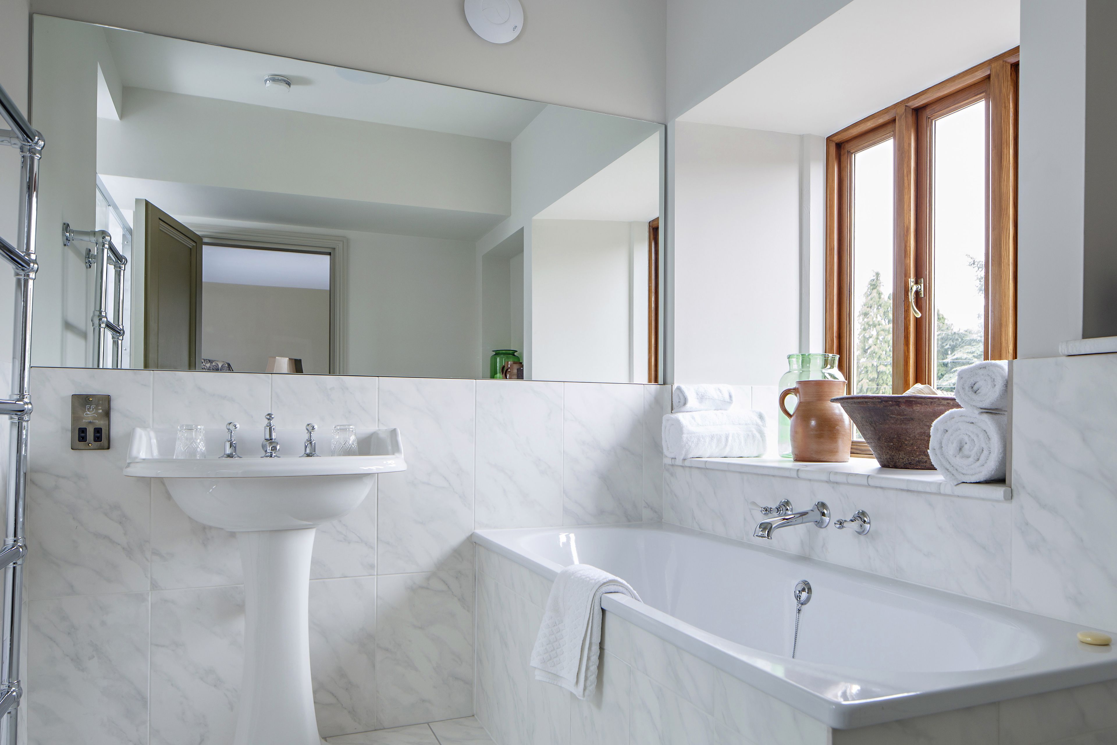 A modern bathroom with a white sink, bathtub, and large mirror.