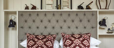 A neatly made bed with patterned pillows, a tufted headboard, and a shelf above with framed items and decorative objects.