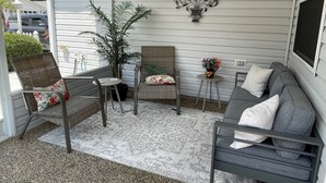 A covered patio area with wicker furniture, a gray sofa, and a decorative metal wall piece.