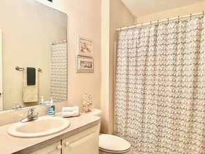 Un baño con lavamanos, espejo, inodoro y cortina de ducha.