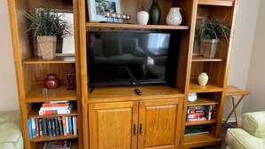 A wooden entertainment center with a television, bookshelves, decorative items, and a remote control.