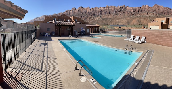 A rooftop pool with a view of mountains, a covered seating area, and a fenced poolside.