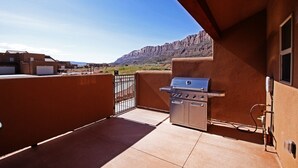 A balcony with a barbecue grill, a view of a mountainous landscape, and a clear sky.