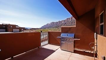 Un balcon avec un barbecue, une vue sur un paysage montagneux et un ciel dégagé.