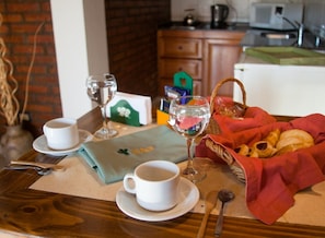Ein Frühstückstisch mit einem Korb voller Croissants, einer Kaffeetasse, einem Weinglas und einer grünen Serviette mit einem Logo.