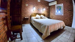 Un dormitorio con pared de ladrillo, cama de madera, mesita de noche y una silla.